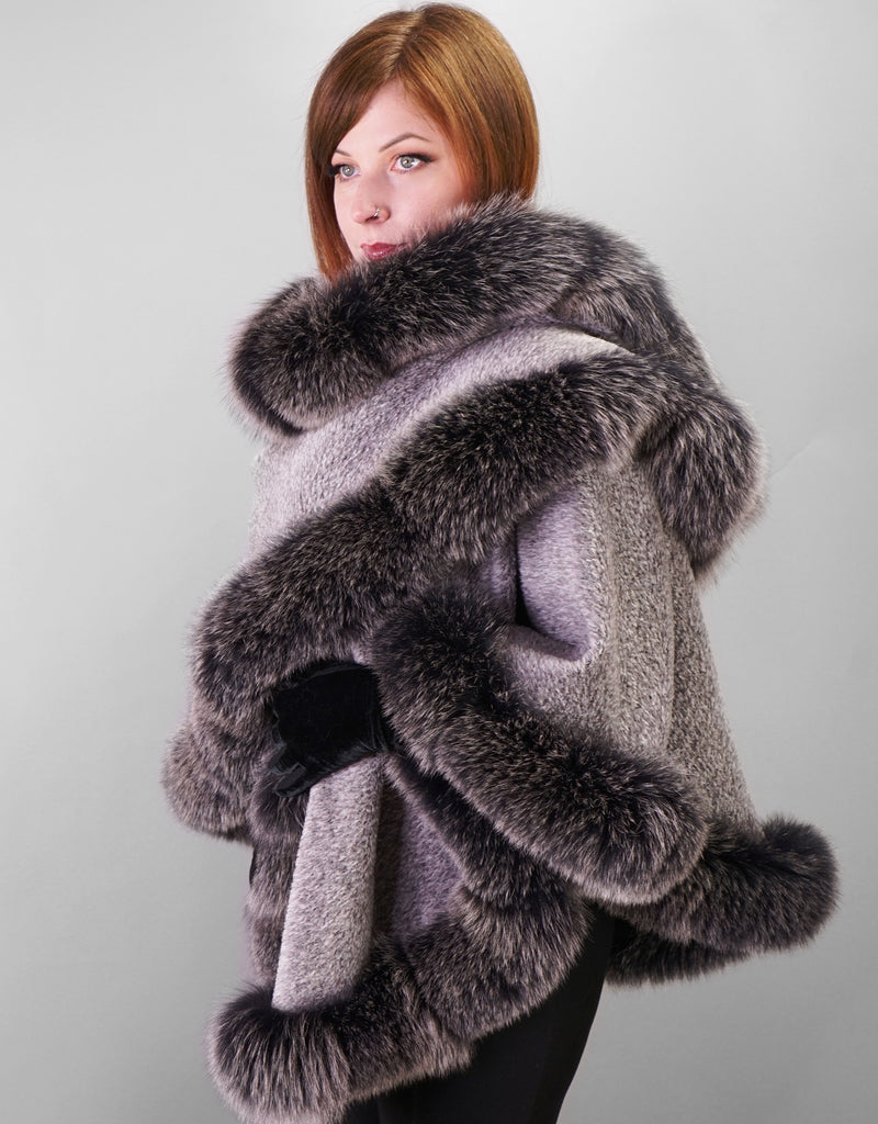 Side view: A red haired woman is wearing a medium length silver cape with Black Snow Fox trim and black leather gloves. In this photo the cape is worn with one side wrapped across the chest and over the opposite shoulder